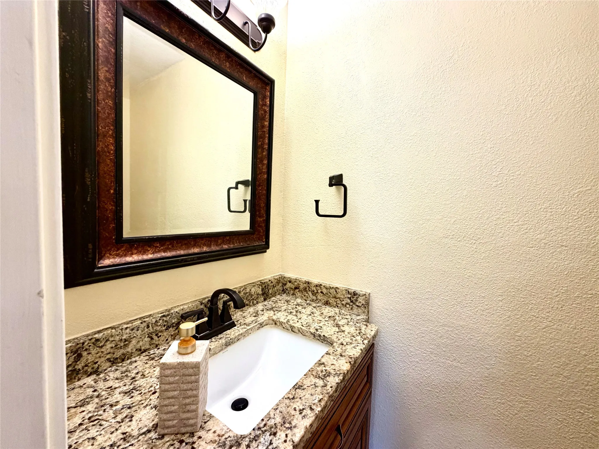 Vanity with a granite-style countertop, undermount sink, and dark bronze faucet