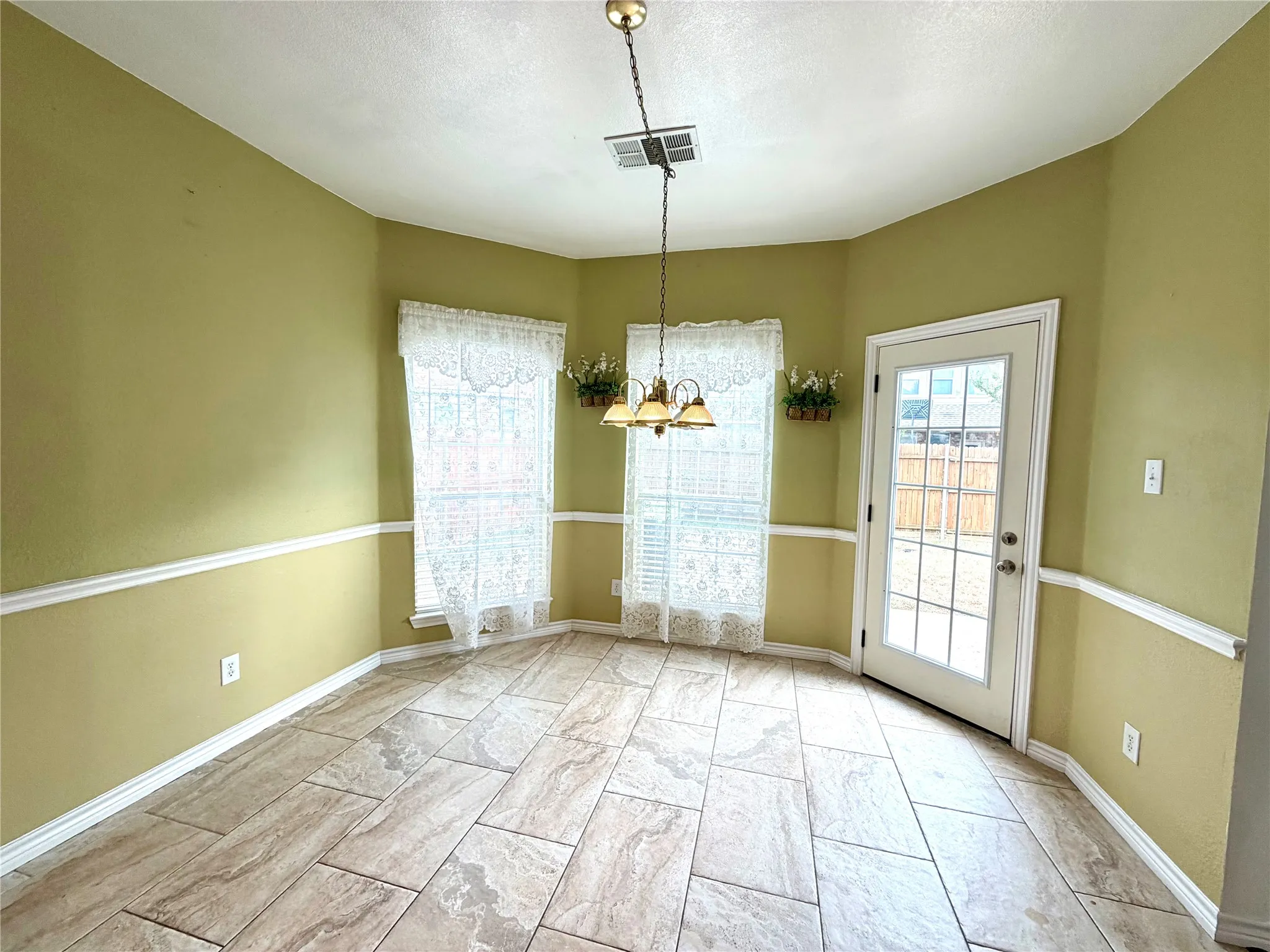 Tiled flooring, two large windows, glass-paned door, and overhead chandelier fixture