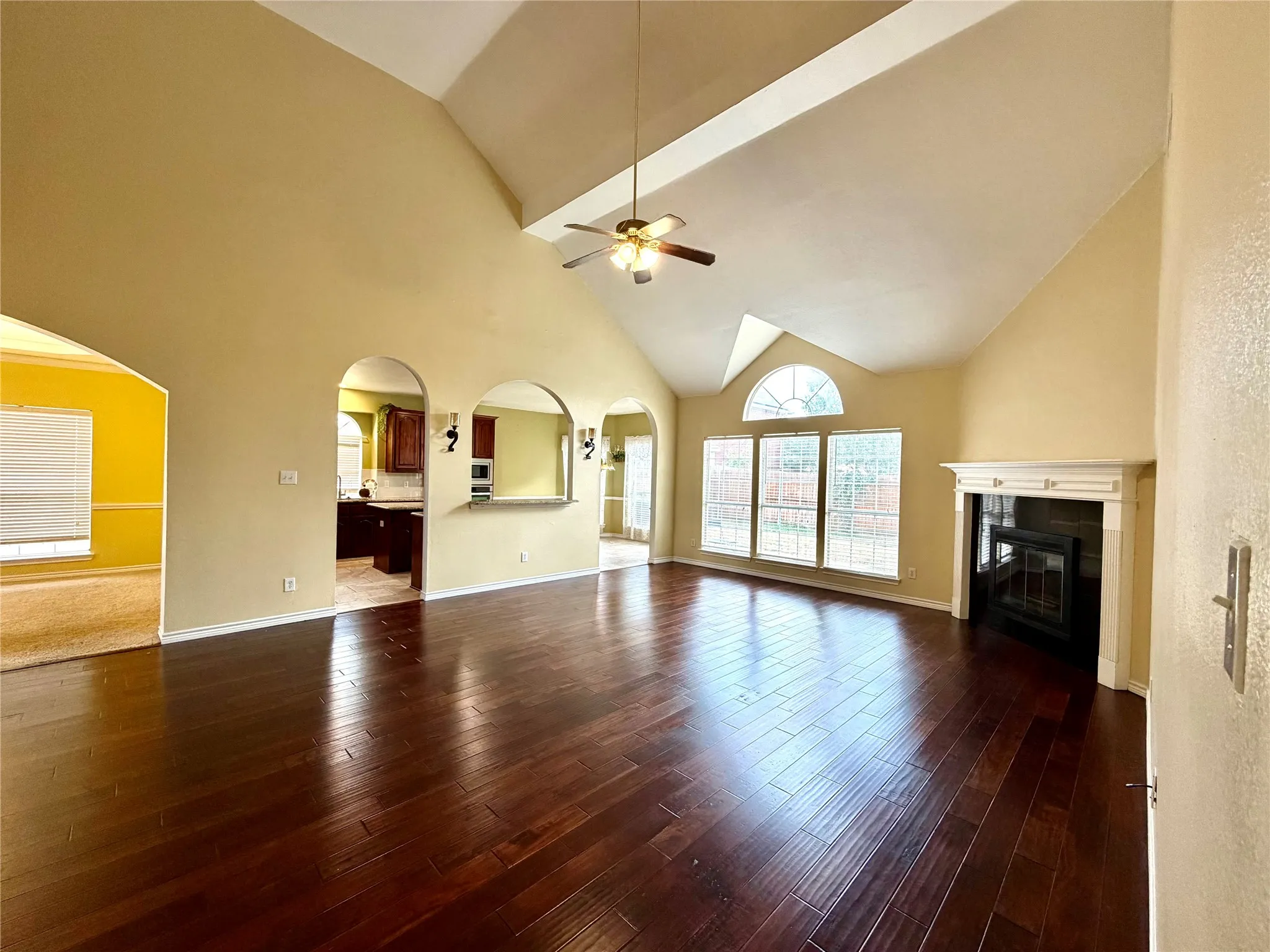 Vaulted ceiling, dark wood-finish flooring, fireplace with mantel, arched doorways, and large windows