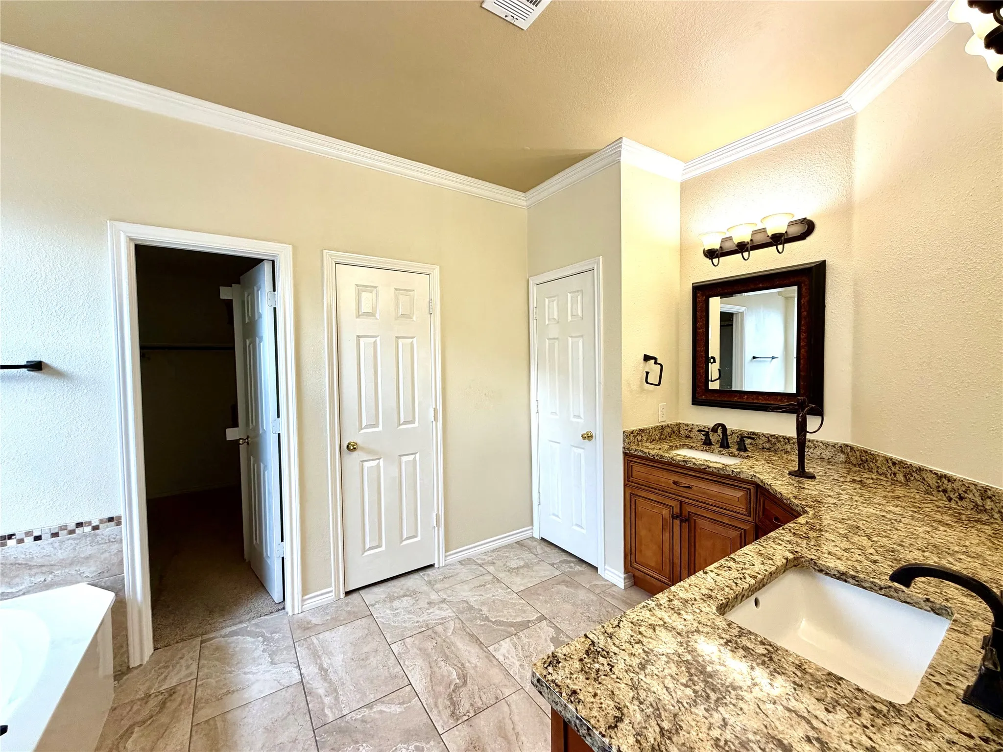 Dual vanity with integrated sinks, granite countertops, wood-finish cabinetry, and tile flooring