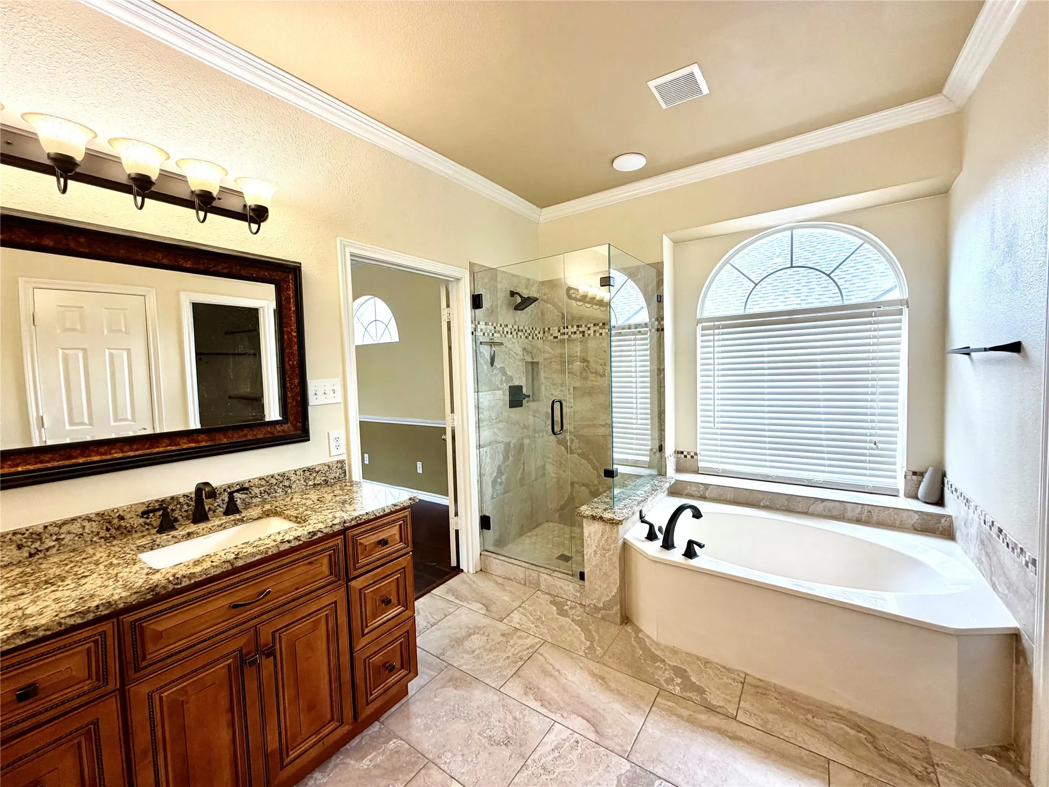 Bathroom featuring a wood-finish vanity with a granite countertop, a built-in soaking tub, a separate glass-enclosed shower, and a decorative arched window