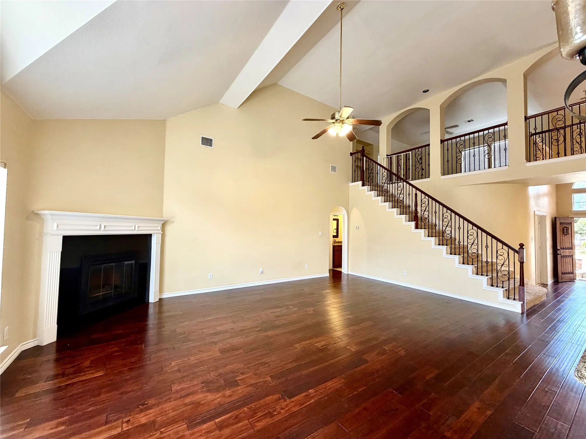 Living space featuring vaulted ceilings, wood-finish flooring, a white mantel fireplace, an ornate staircase with wrought iron balusters, and a ceiling fan