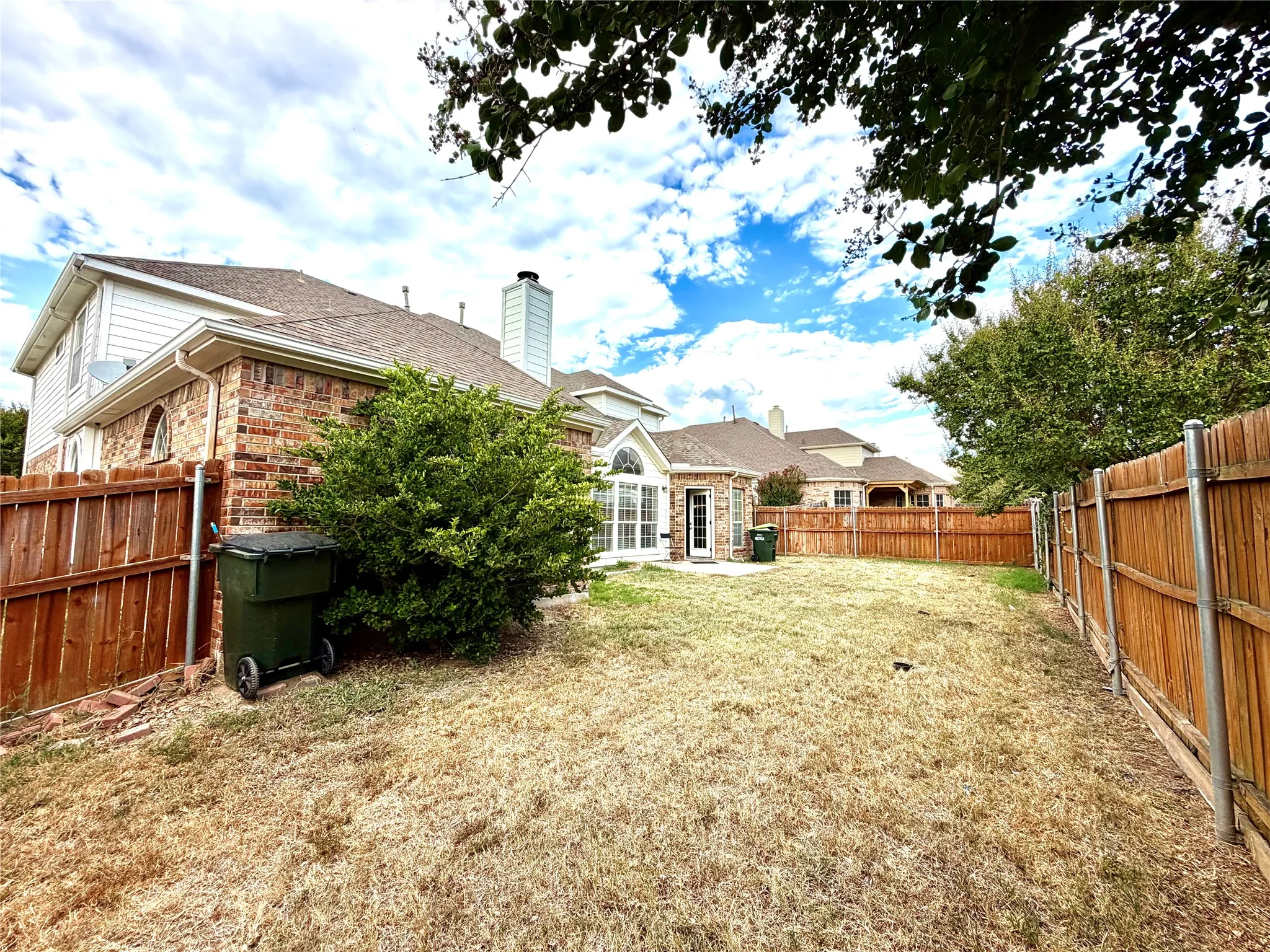 Expansive backyard featuring a wood privacy fence and a brick-clad exterior