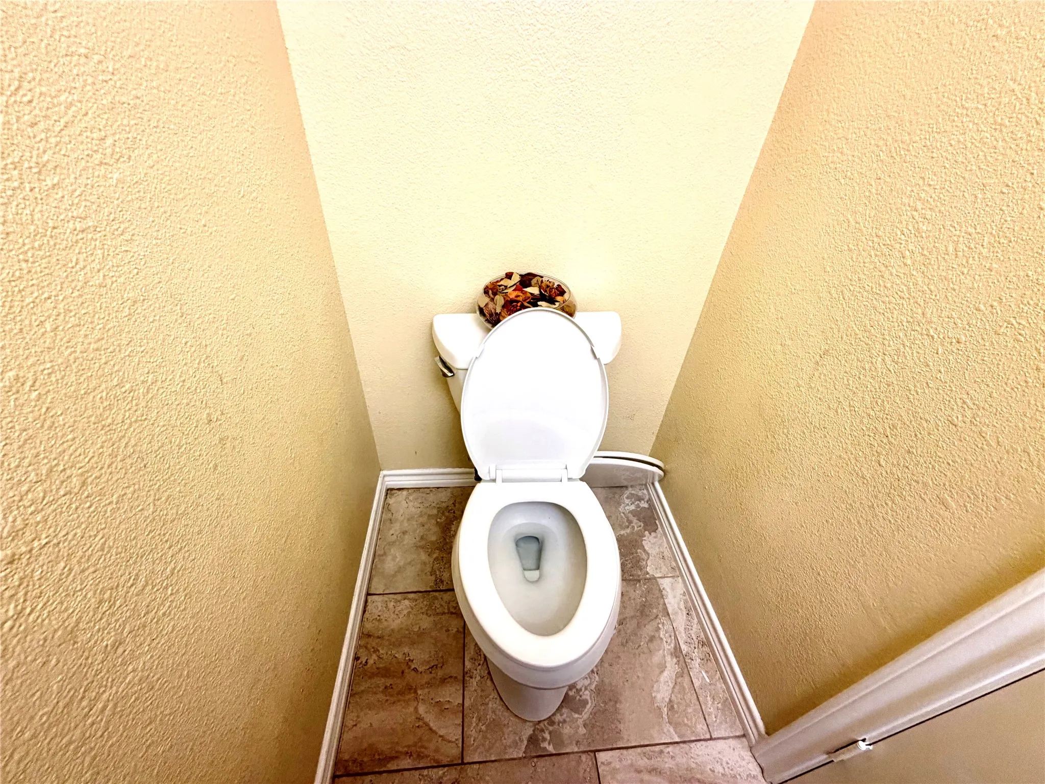 White commode with a standard tank, set against textured walls, with neutral-toned floor tiling