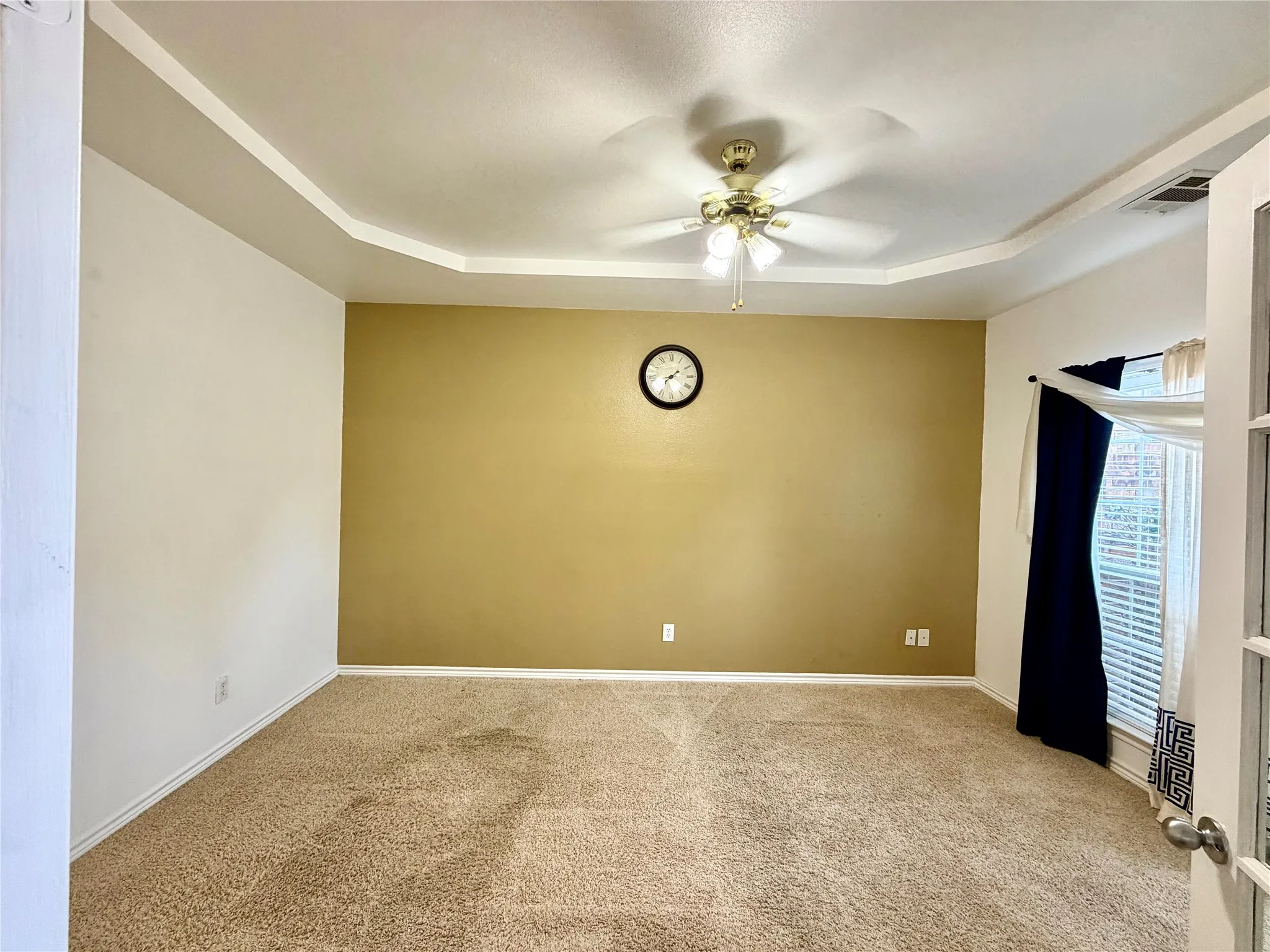 Tray ceiling with a ceiling fan light fixture, carpet flooring, and a window with blinds