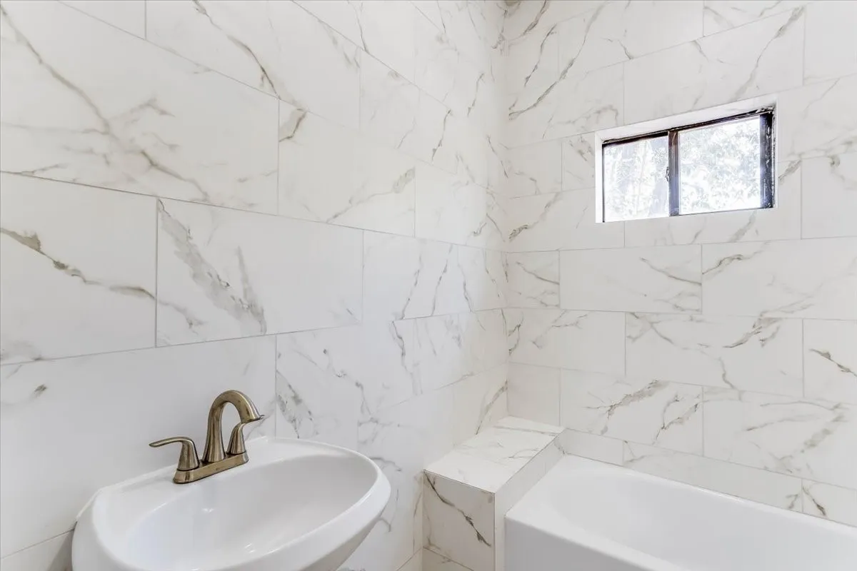 White marbled tile walls, pedestal sink, and bronze-finish faucet