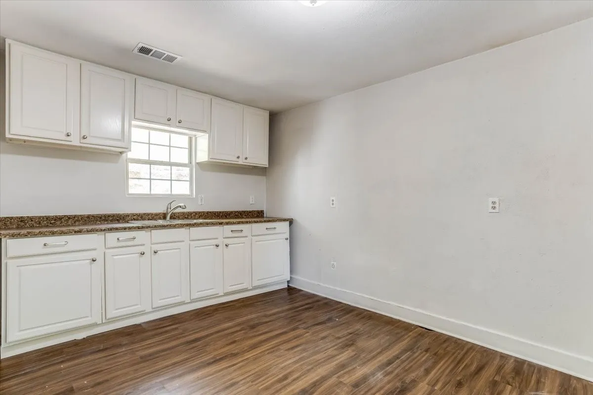 White cabinetry with brushed nickel hardware, speckled countertops, stainless steel sink, wood-finish flooring, and a large window Unit 4
