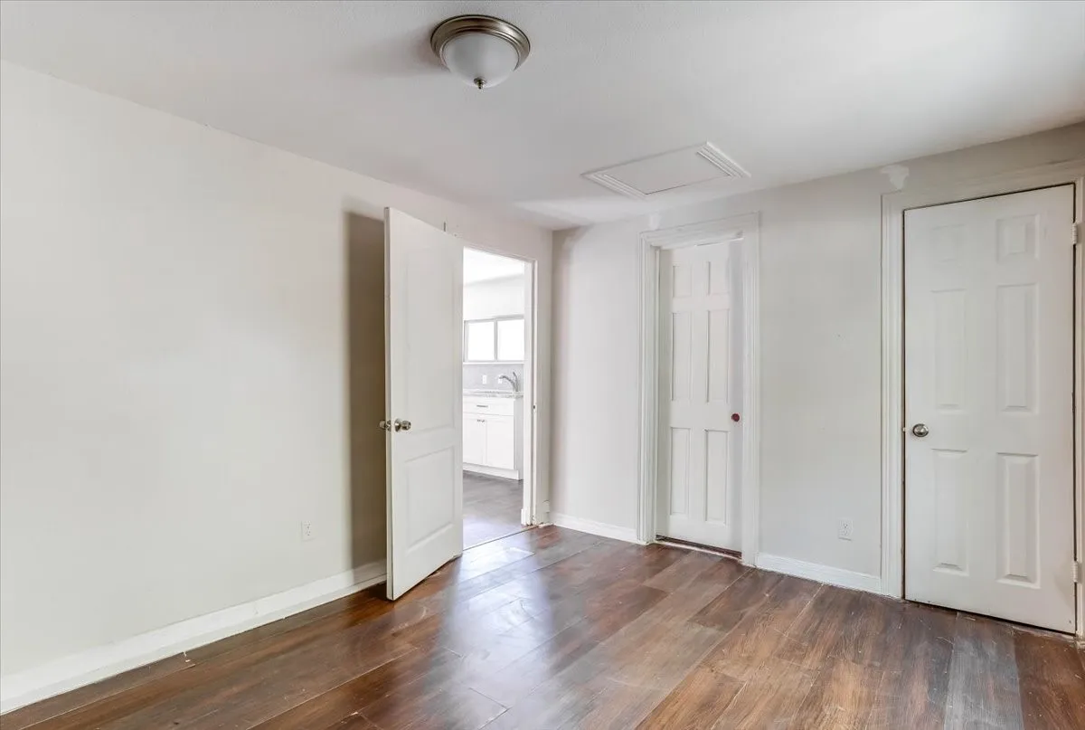 Wood-finish flooring with white baseboards, white walls, and a ceiling-mounted light fixture Unit 3