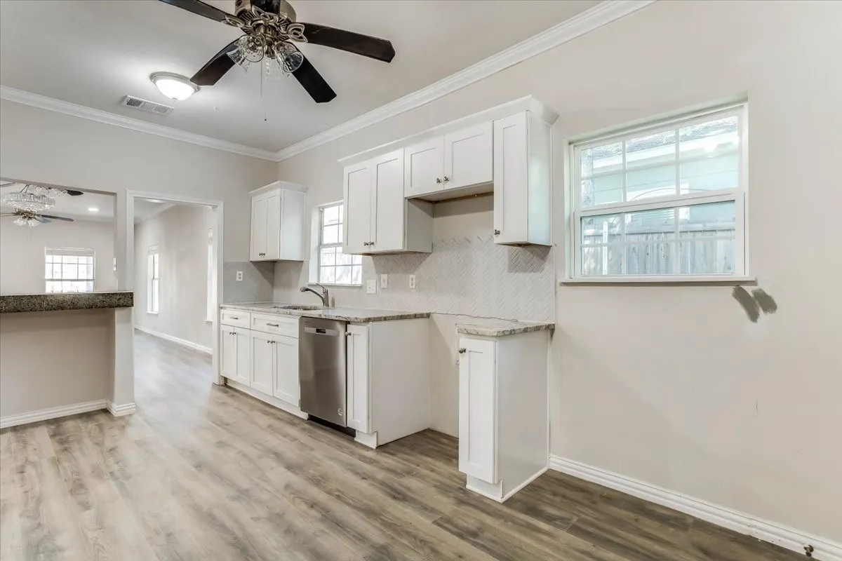 Kitchen featuring white cabinetry, light-toned wood-finish flooring, stainless steel dishwasher, speckled countertops, and a white subway tile backsplash