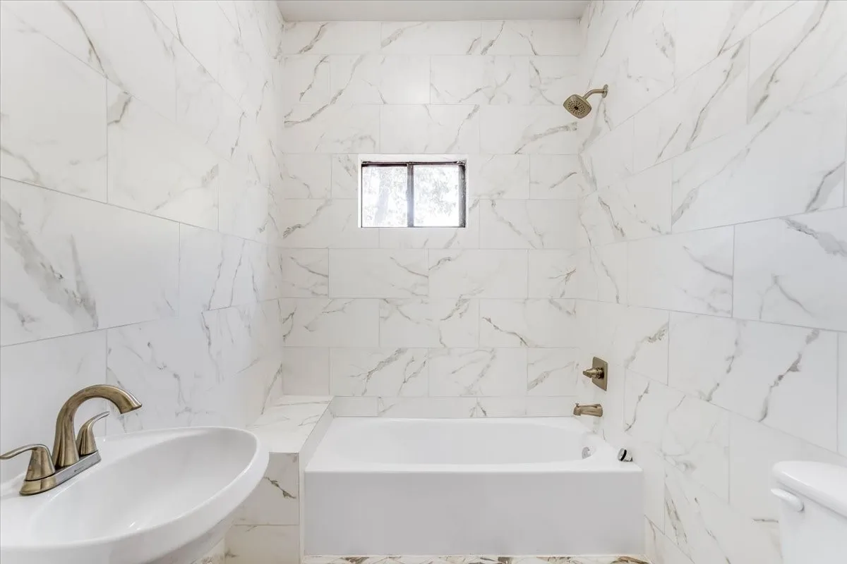 Bathroom featuring large format wall tiles, a white bathtub, and bronze-finish fixtures