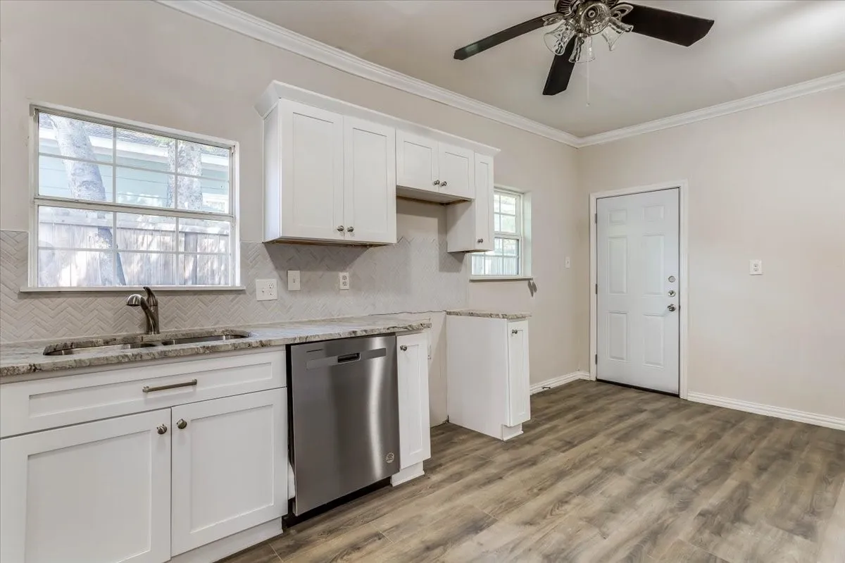 White shaker cabinetry, stone countertops, stainless steel dishwasher, wood-finish flooring, and crown molding