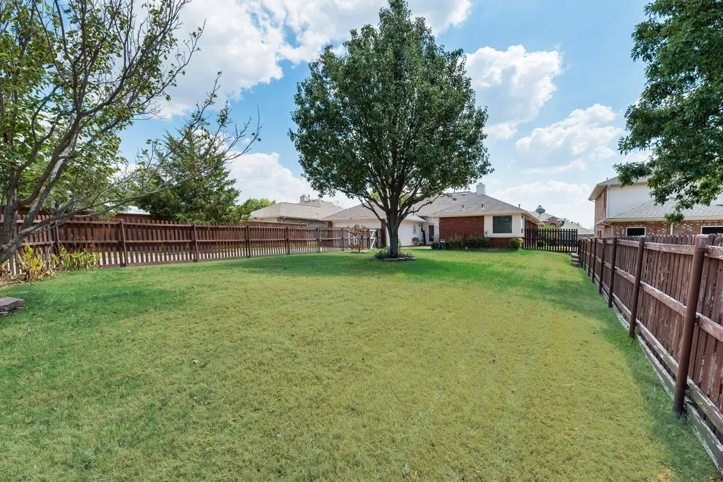 Expansive green lawn with mature trees and a perimeter wood fence