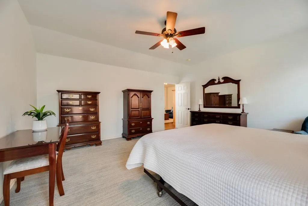 Vaulted ceiling, ceiling fan, white walls, light-colored carpet, and an interior doorway
