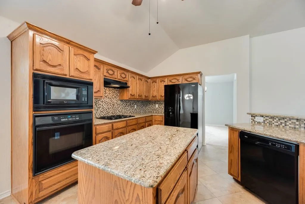 Kitchen featuring wood cabinetry, granite-finish countertops, a tile backsplash, and integrated black appliances