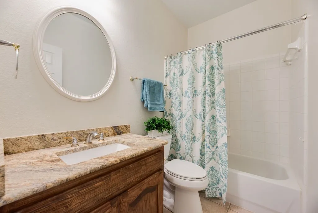Full Bathroom featuring a vanity with an integrated sink, a polished stone countertop, a circular framed mirror, and a tiled shower and tub