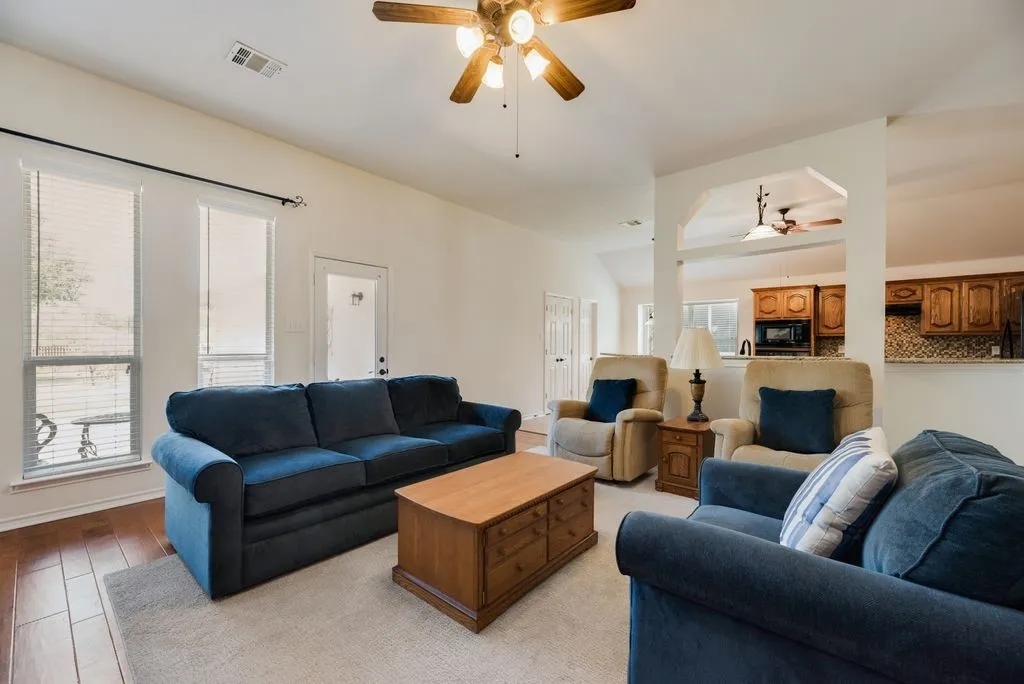 Hardwood-style flooring, white walls, arched entryway, ceiling fan with integrated lighting, and multiple windows