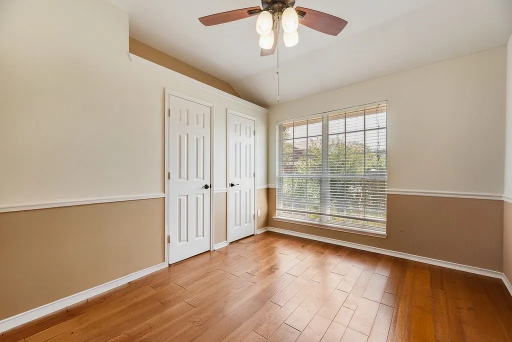 Bedroom 2 Wood-finish flooring, two-tone wall treatment with chair rail, and a ceiling fan with integrated lighting