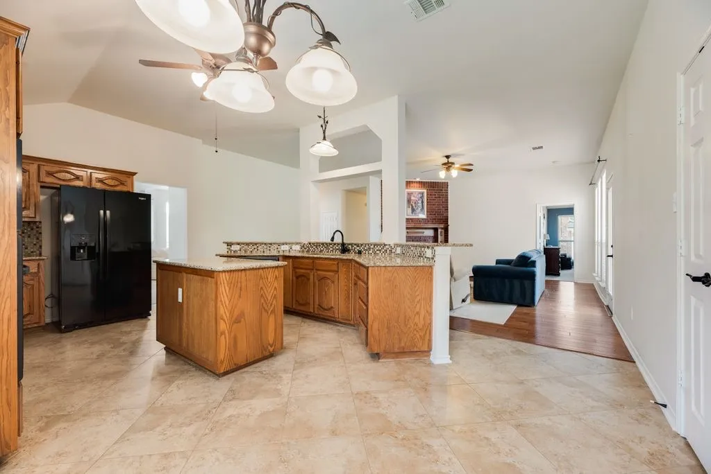 Kitchen featuring an island, wood cabinetry, granite countertops, and tile flooring