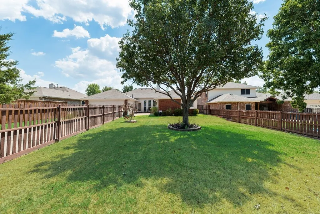Expansive grassy yard with a mature shade tree and wood fencing