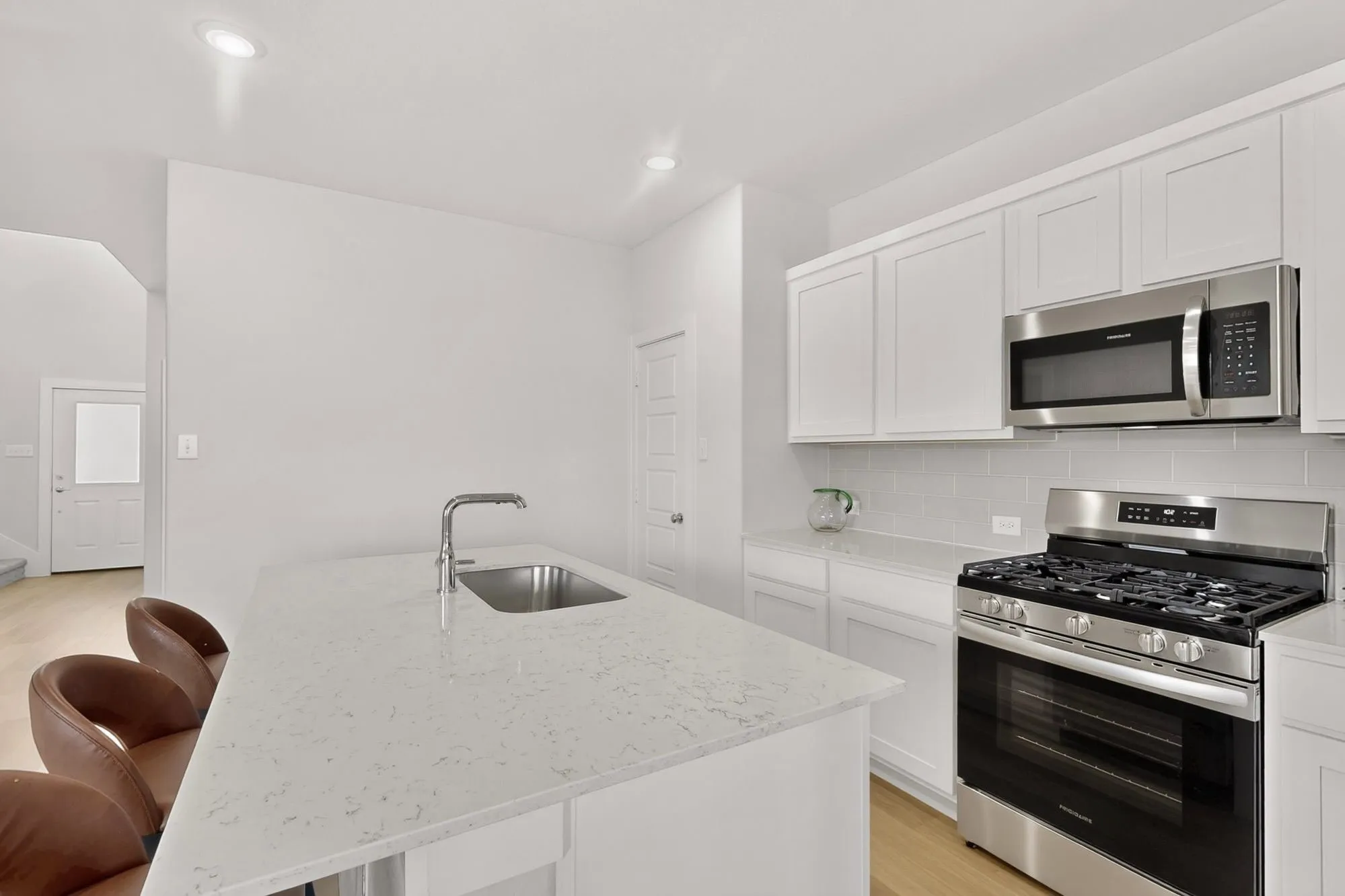 Kitchen with a white quartz island, stainless steel sink, stainless steel gas range, stainless steel microwave, and white shaker-style cabinetry
