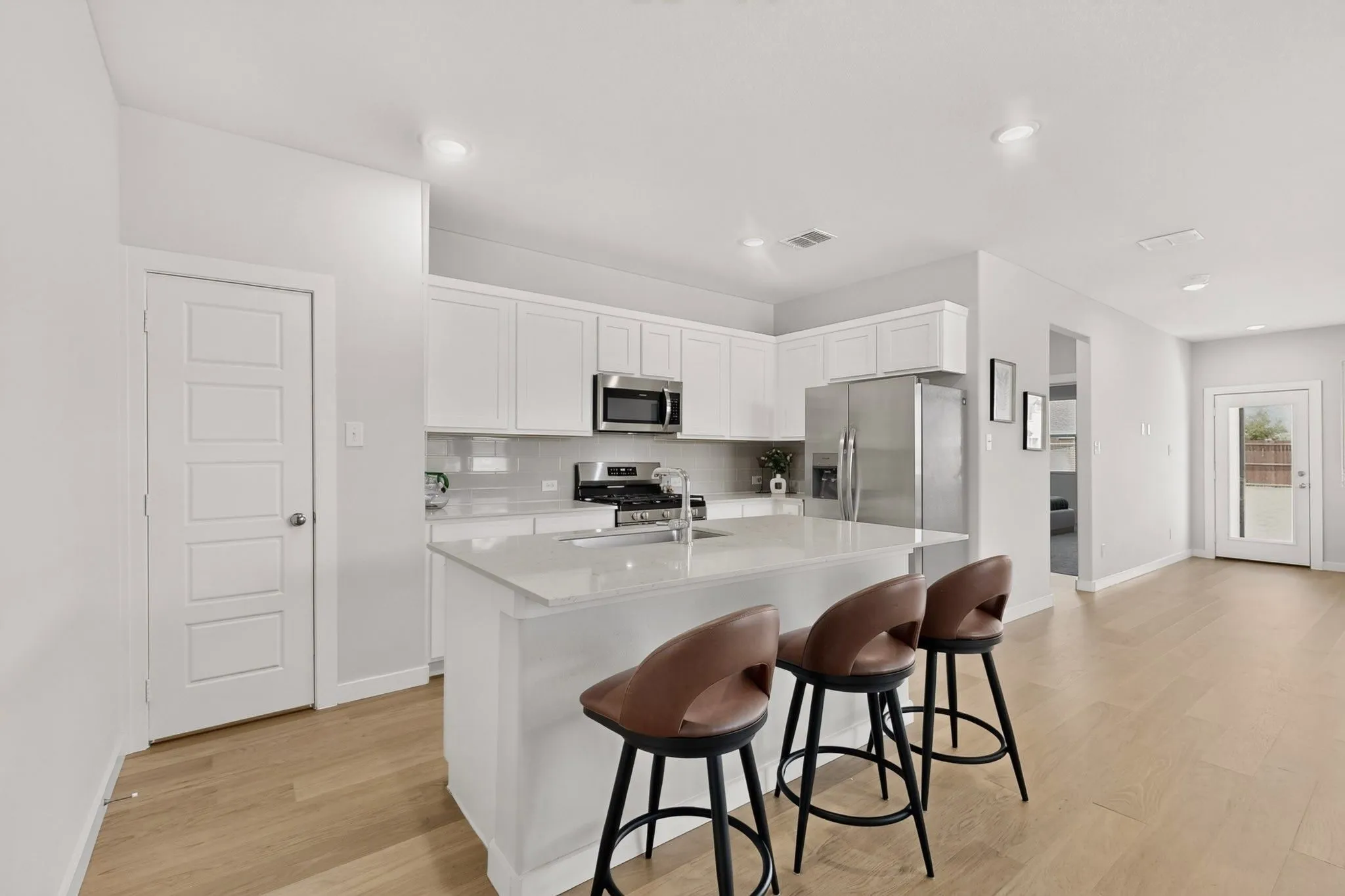 Modern kitchen featuring a central island, stainless steel appliances, white cabinetry, a light-toned backsplash, and wood-finish flooring