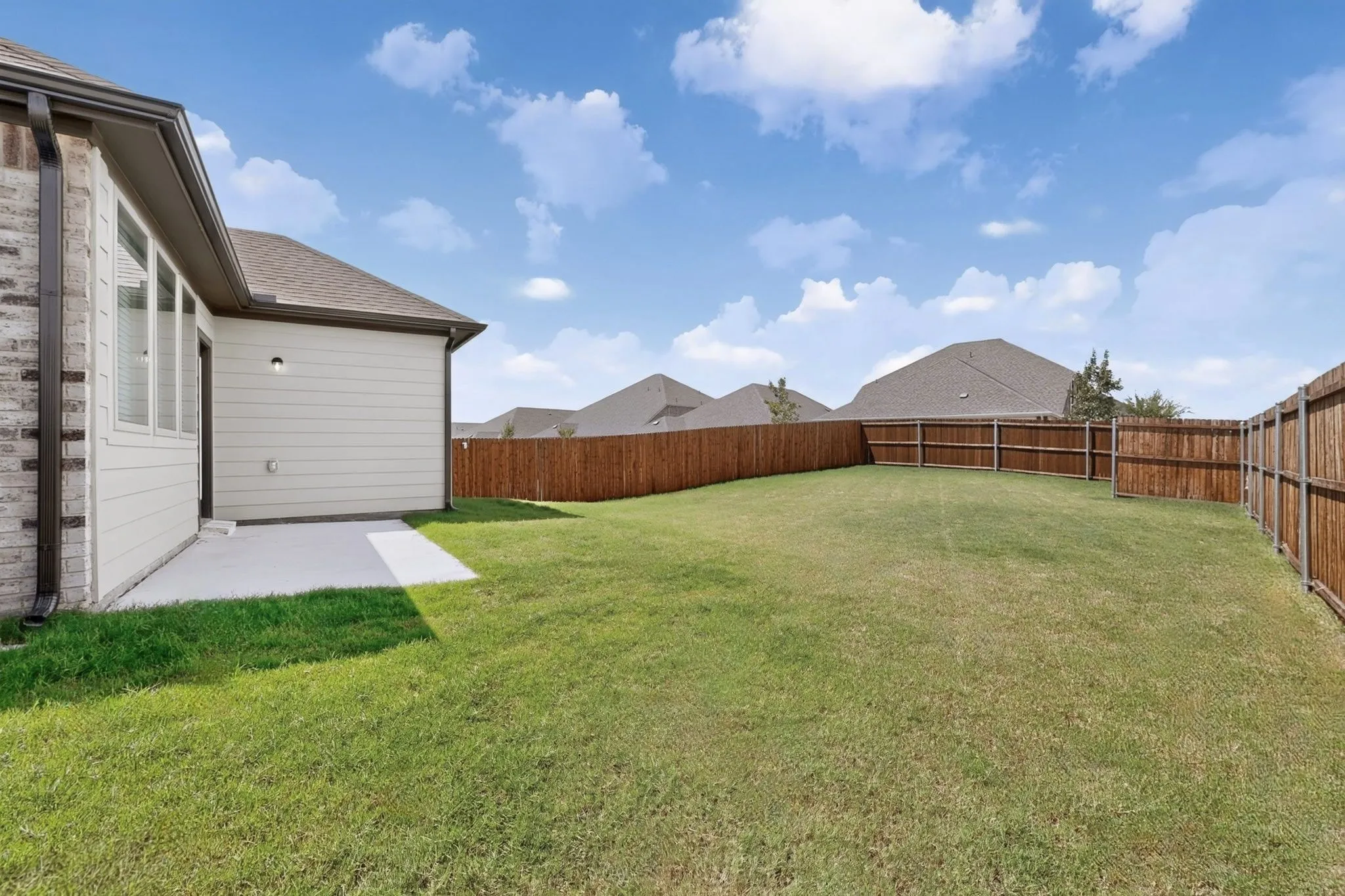 Expansive backyard featuring a manicured lawn, full perimeter privacy fencing, and a concrete patio