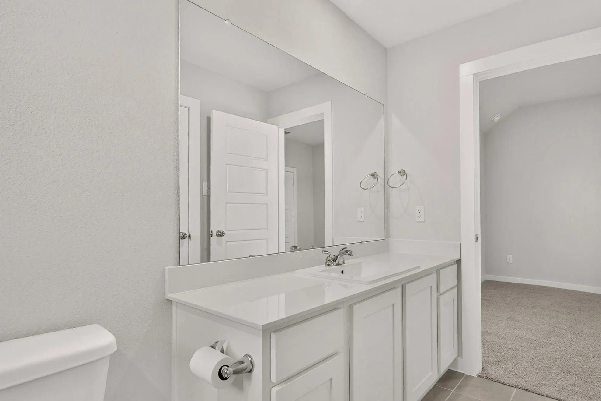 Bathroom featuring a spacious vanity with an integrated sink and chrome faucet, a large mirror, and tiled flooring