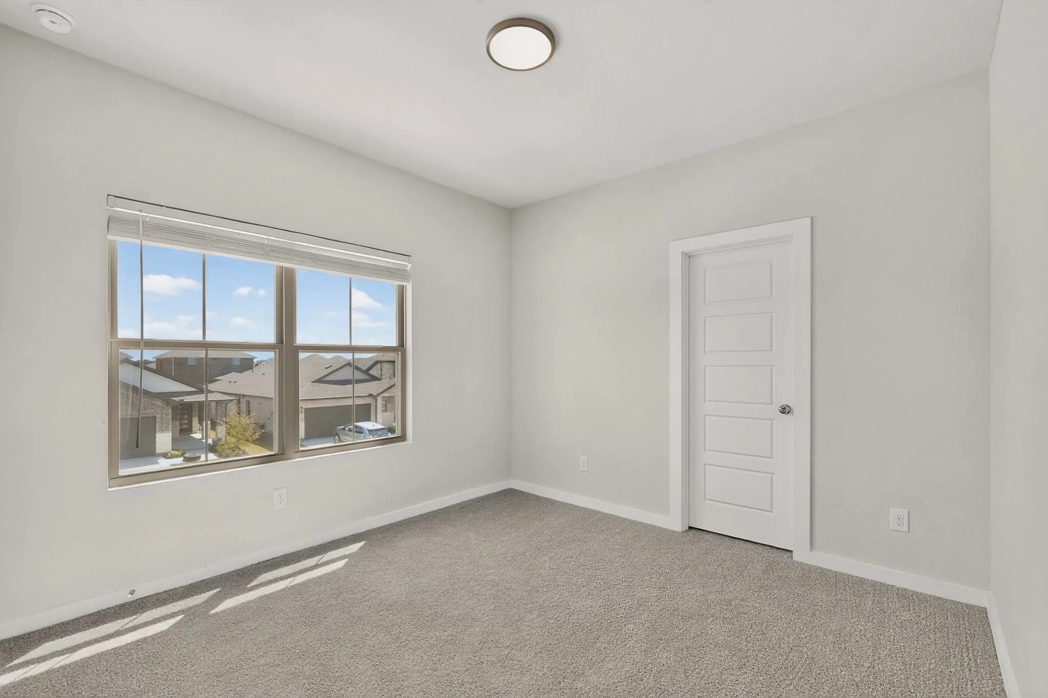 Carpeted flooring, white five-panel interior door, flush mount ceiling light, and a large window with blinds