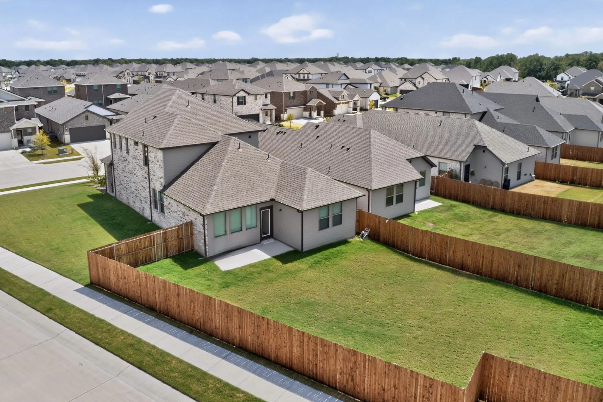 Expansive grassy yard with wood fencing, featuring a concrete patio, and a two-story residence with a stone and siding exterior