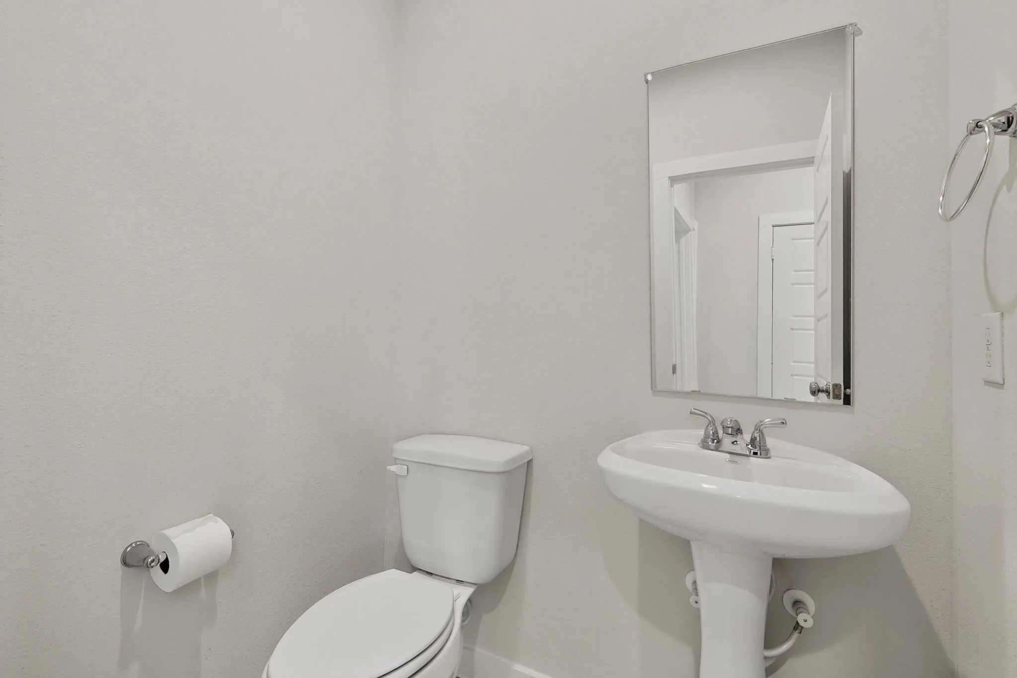 Pedestal sink with chrome-finish faucet, wall-mounted mirror, and white toilet