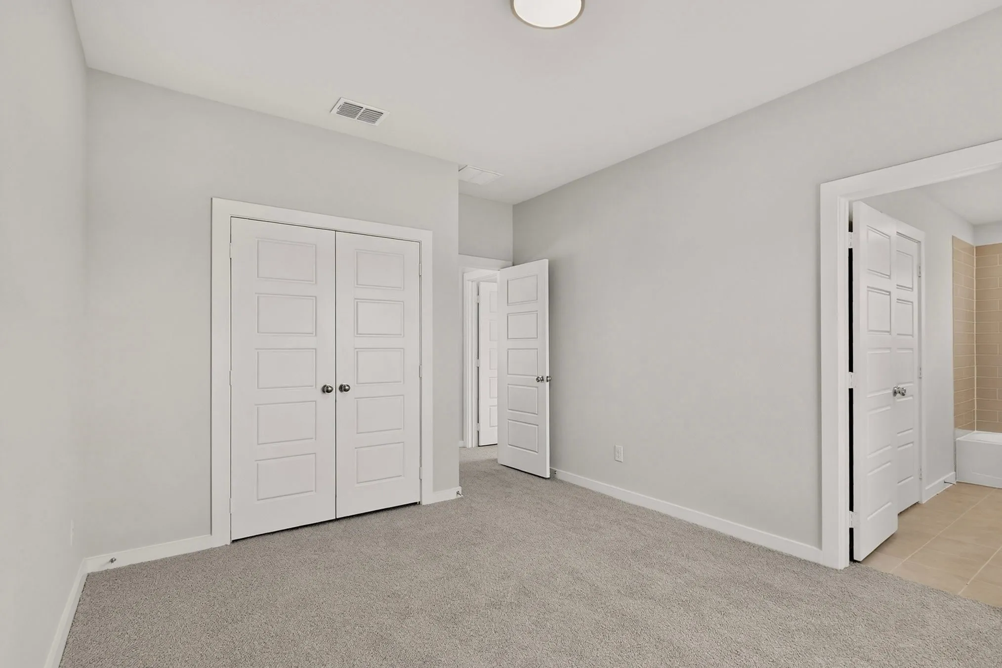 Light gray wall paint, gray carpet flooring, white paneled double doors, white ceiling, and a flush mount ceiling light