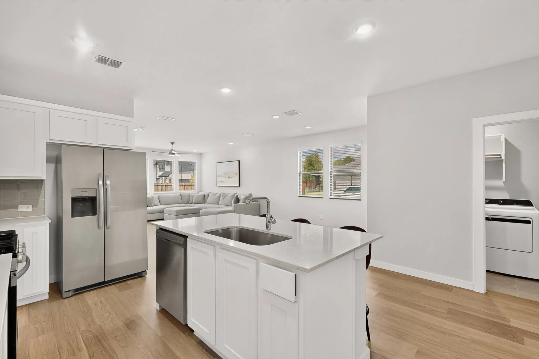 Kitchen with white cabinetry, stainless steel appliances, a center island with sink, and wood-finish flooring