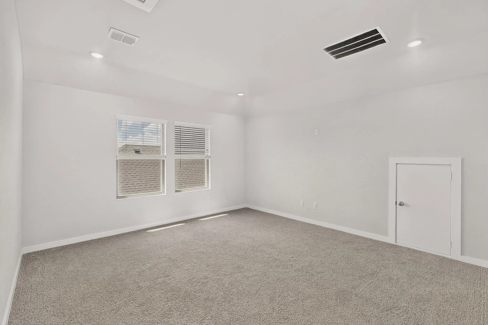 Bright, open room featuring neutral carpet flooring, recessed ceiling lighting, and multiple windows with cellular shades providing natural illumination