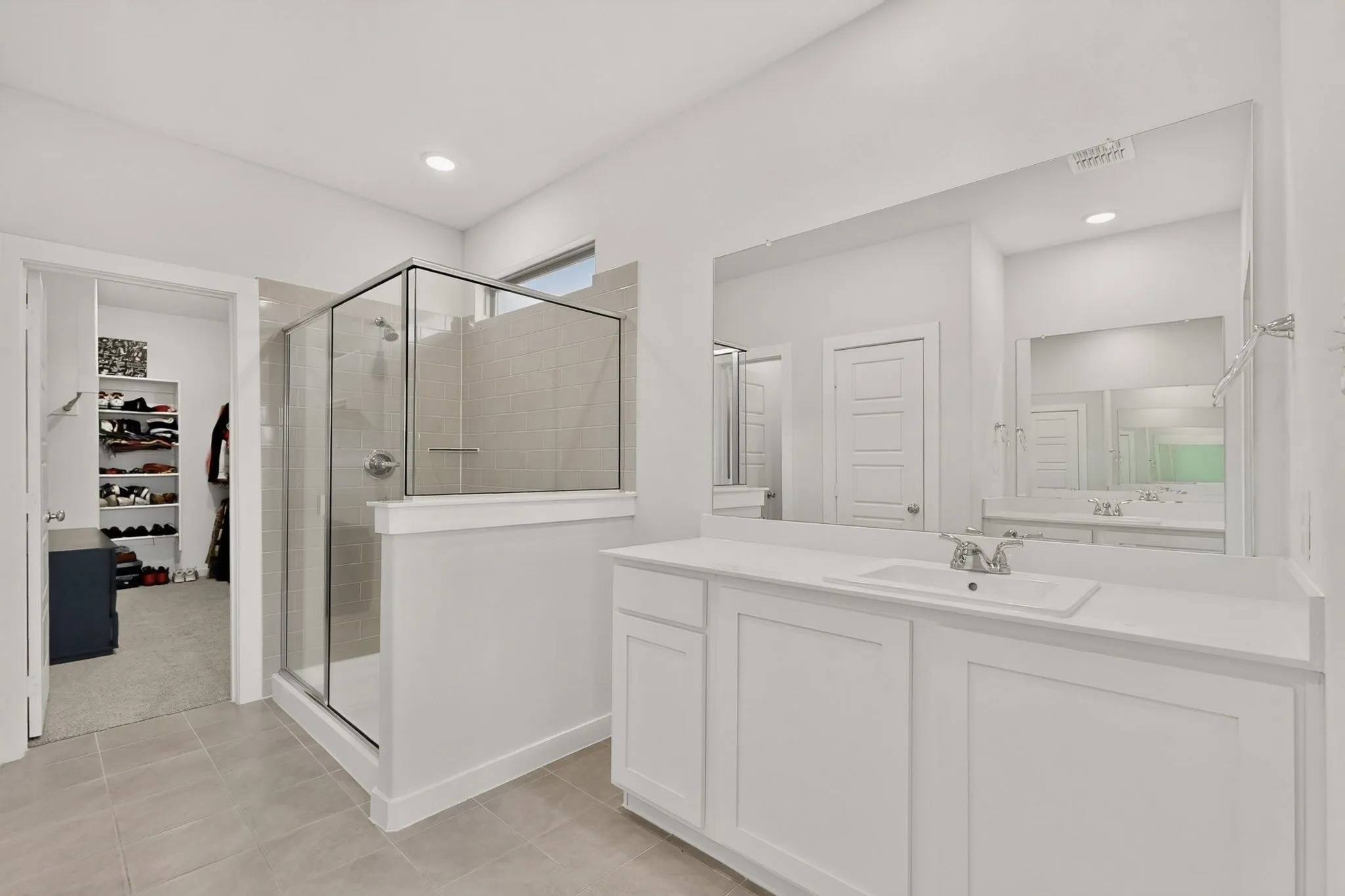 Bathroom featuring a glass-enclosed shower with tiled walls, a wide vanity with an integrated sink, a large wall-mounted mirror, and tile flooring