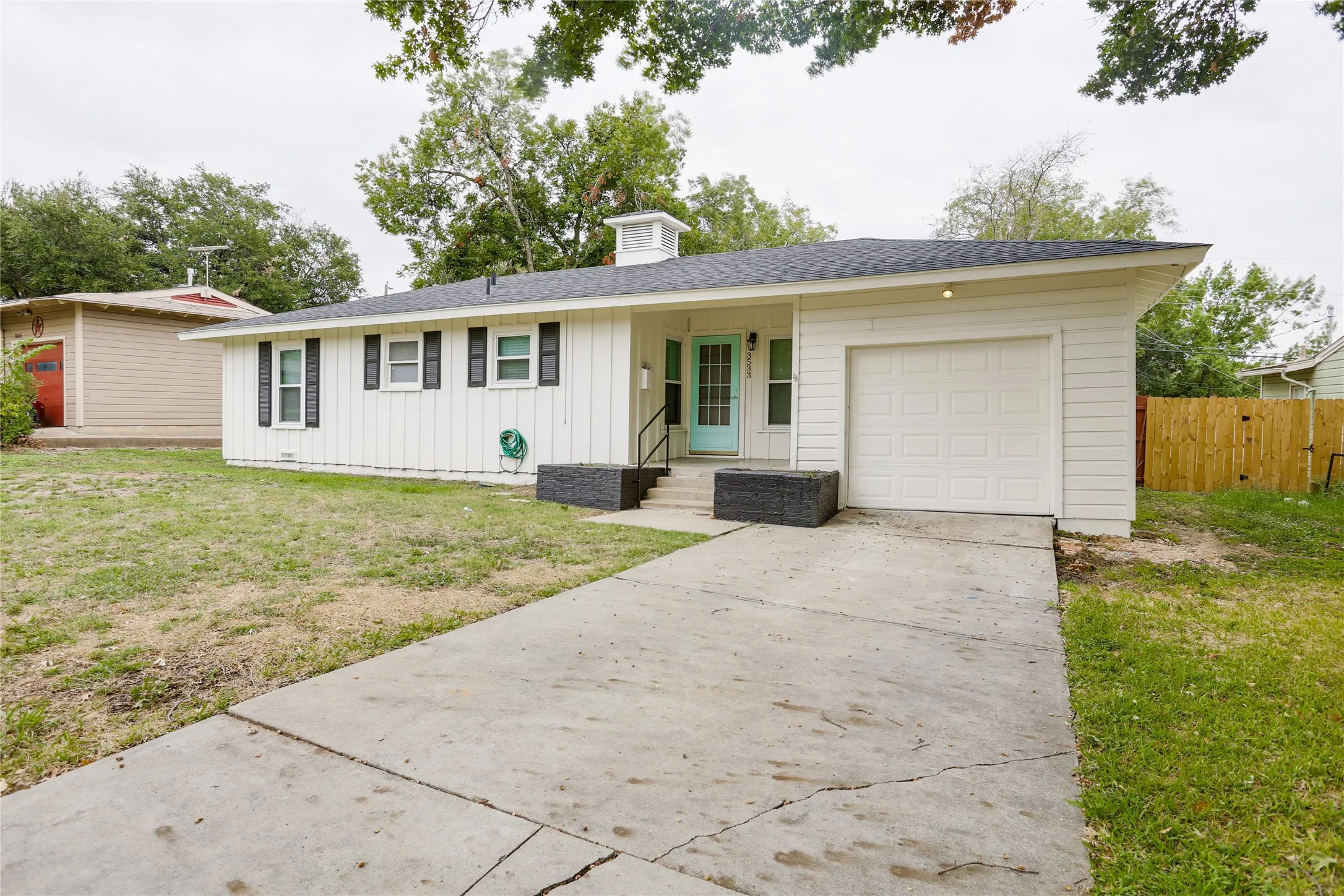 White vertical siding, black roof, black window shutters, attached garage, and concrete driveway