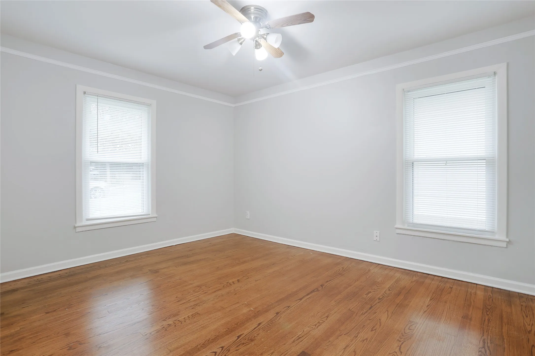 Hardwood flooring, painted walls, crown molding, two windows, and a ceiling fan with integrated lighting