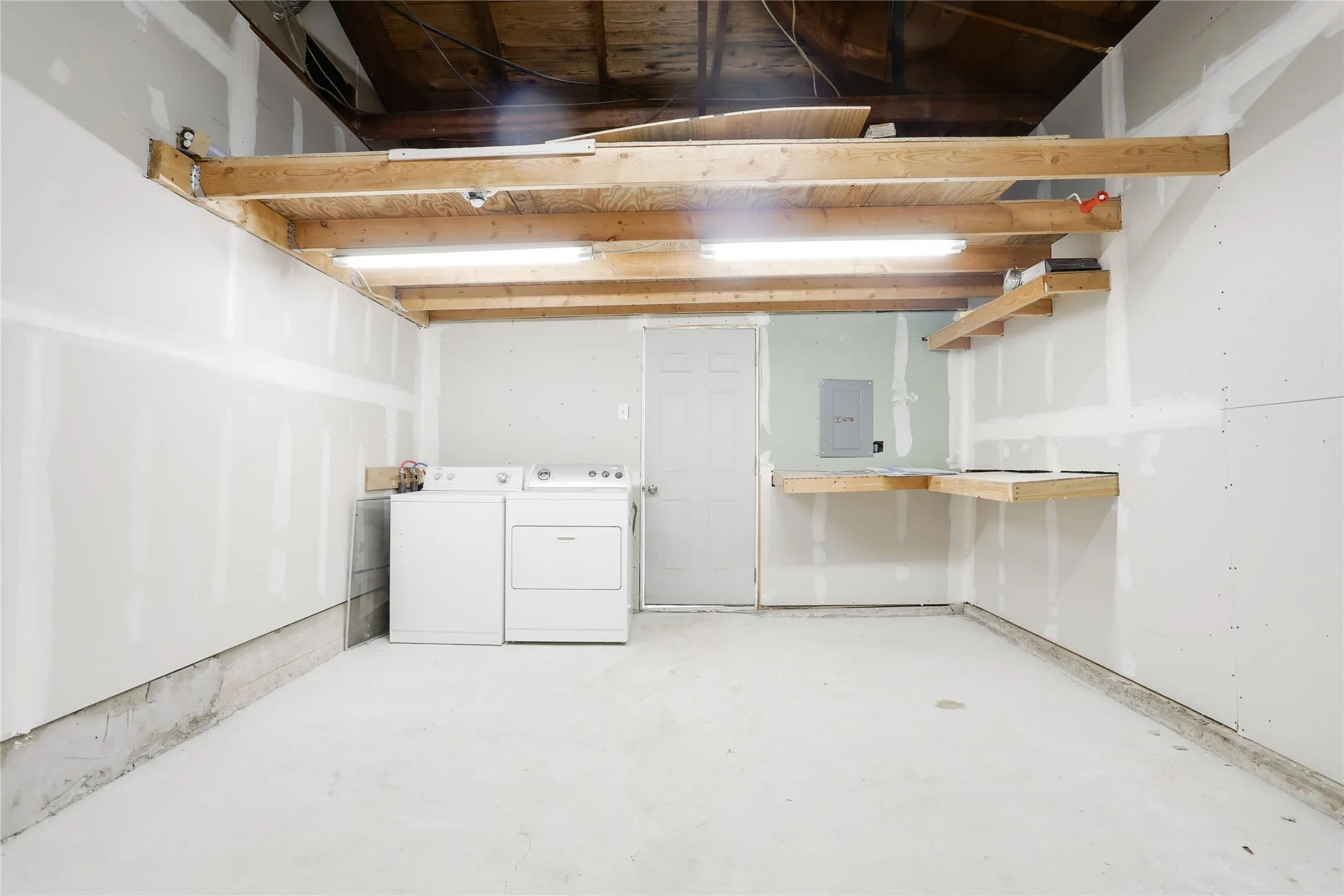 Open utility space with exposed wood beams, overhead fluorescent lighting, and a durable concrete floor