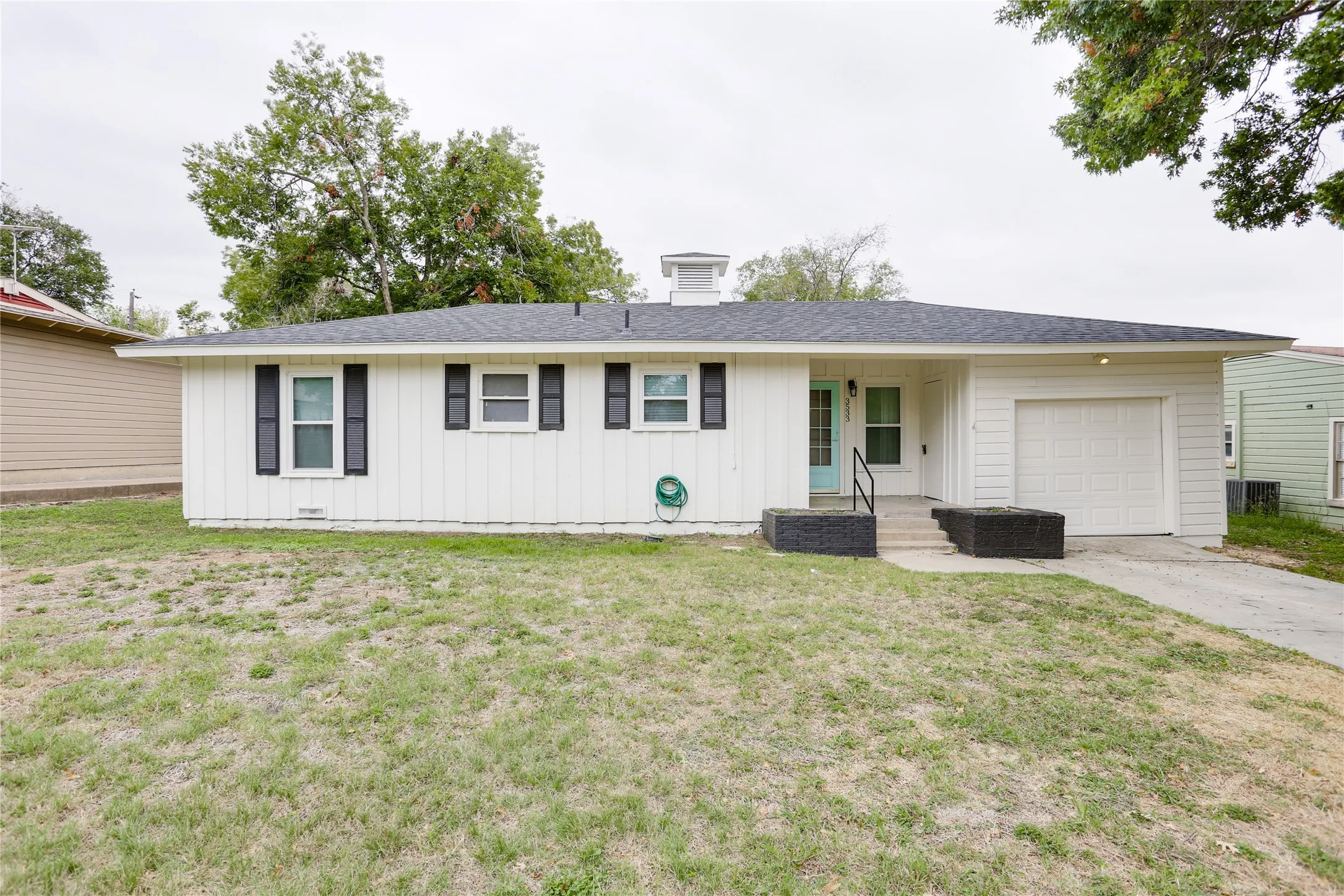White siding exterior, dark shingle roof, attached garage, and concrete driveway