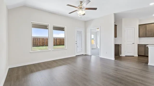Unfurnished living room with ceiling fan, baseboards, and dark wood-style floors