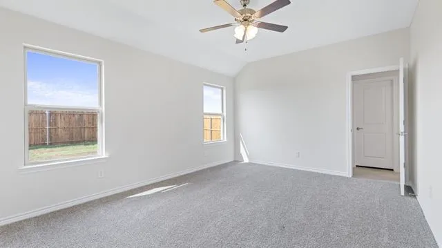 Carpeted spare room featuring vaulted ceiling, a ceiling fan, and baseboards