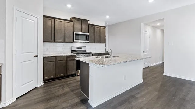 Kitchen featuring appliances with stainless steel finishes, dark brown cabinetry, dark wood-style flooring, and a sink