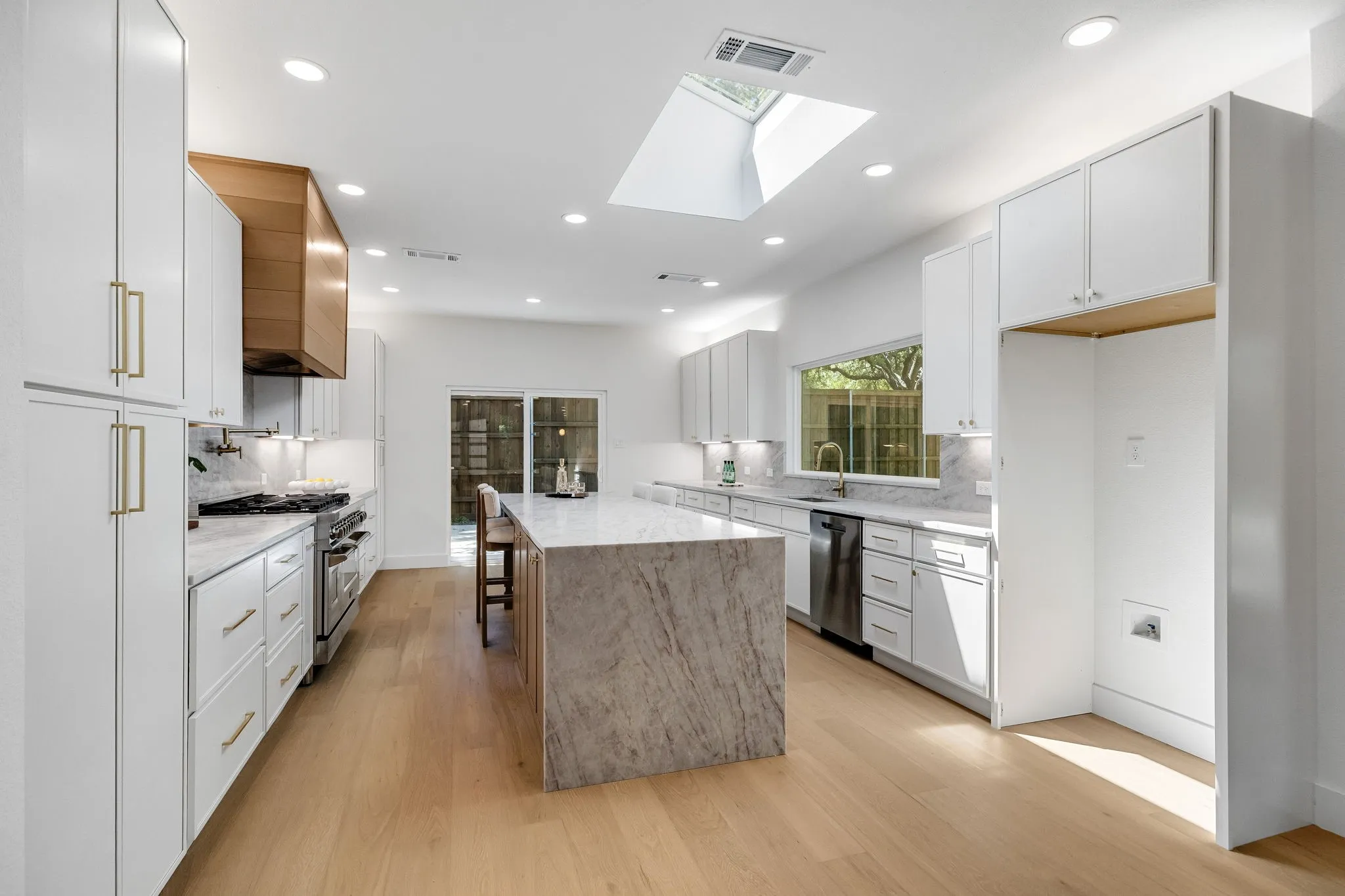 4402 Briargrove-Designer kitchen featuring an oversized central island, overhead skylight, wide-plank white oak flooring, shaker white cabinetry, stainless steel appliances