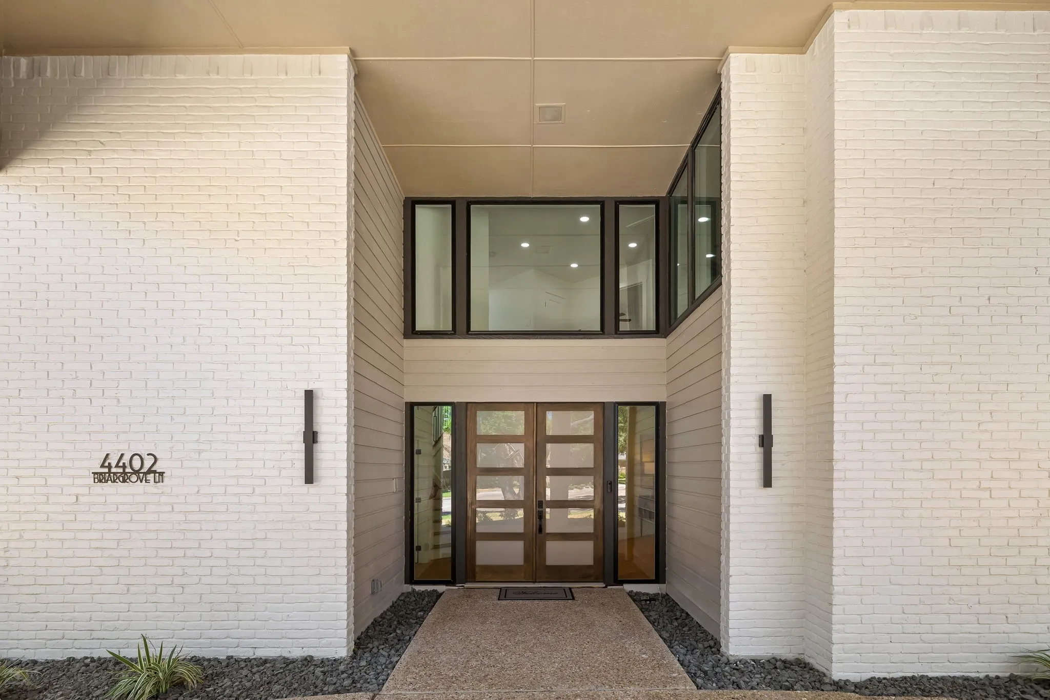 4402 Briargrove- White brick exterior with vertical siding accents, prominent transom windows, and a striking double-door entry with dark-framed detailing.