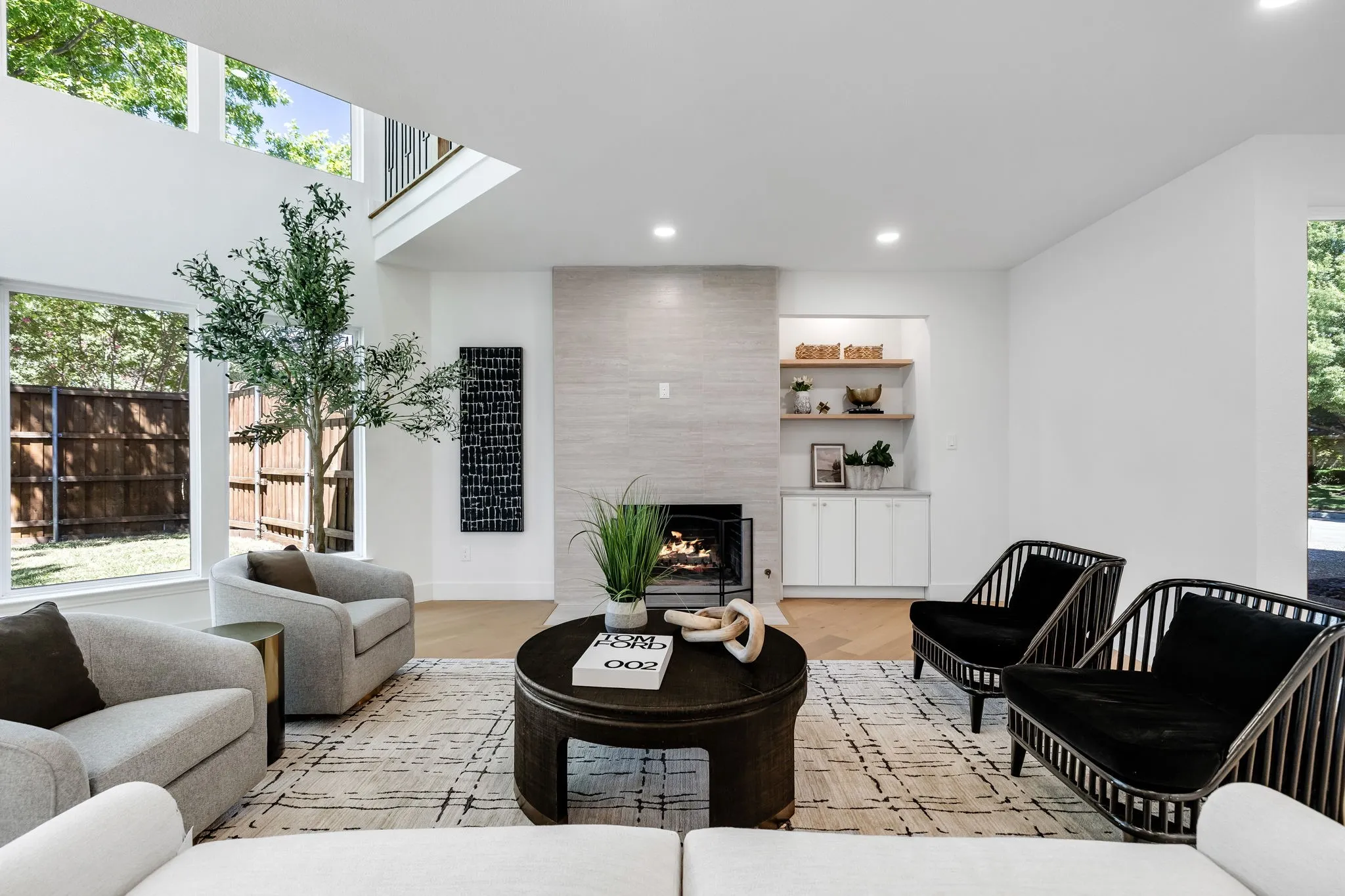 4402 Briargrove-Sunlit living space featuring high ceilings, wide-plank white oak flooring, a stone-clad fireplace, and custom built-in shelving and cabinetry.