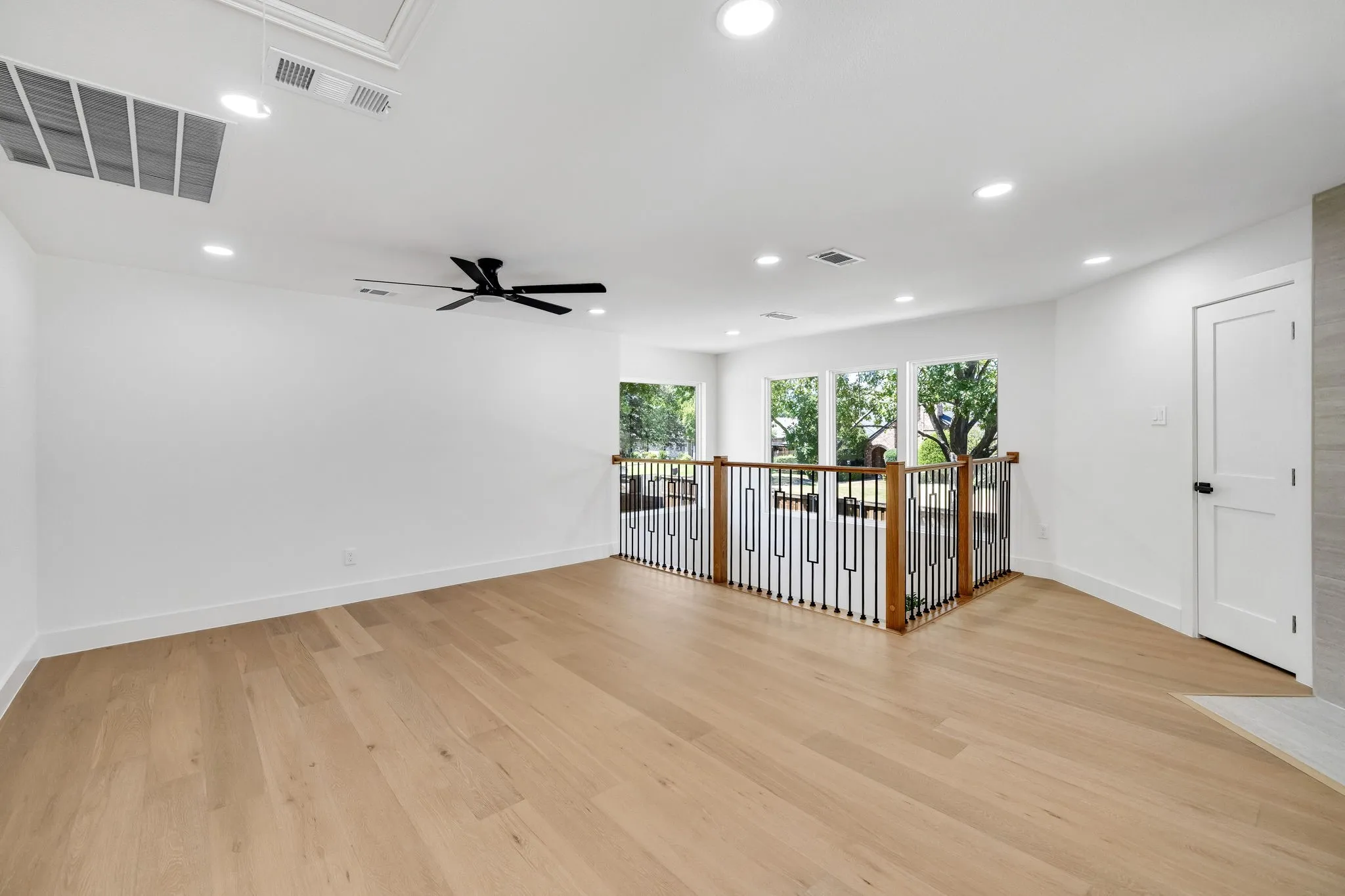4402 Briargrove-Light wood-finish flooring, recessed lighting, ceiling fan, white paneled door with black hardware, and an open railing with wood and black metal balusters