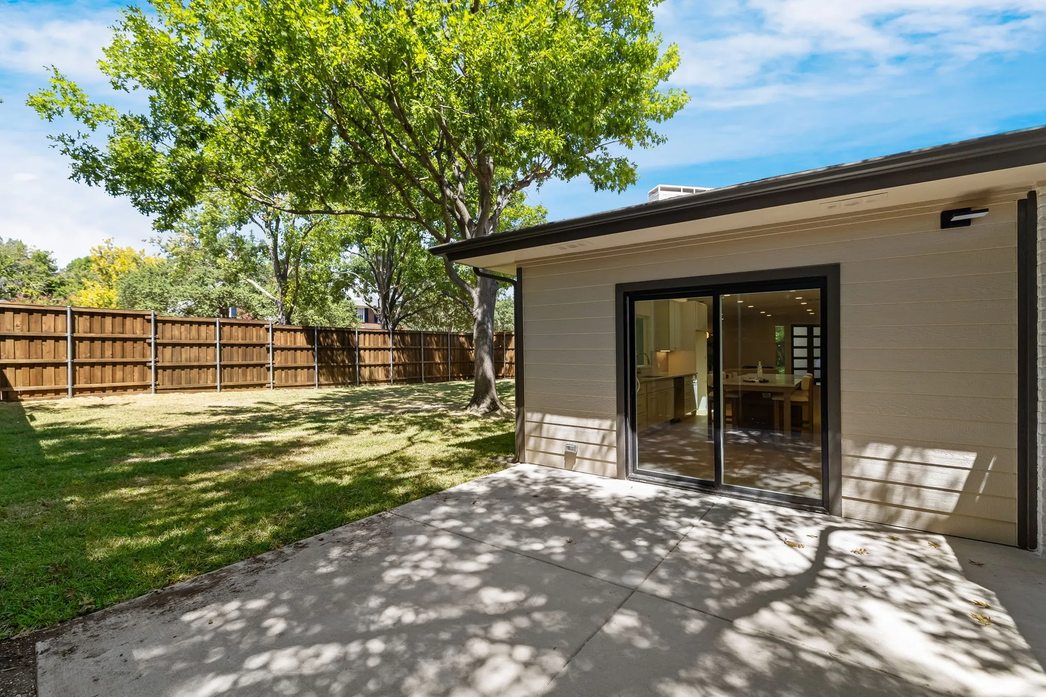 4402 Briargrove-Expansive backyard featuring a manicured lawn, wood privacy fence, mature trees, and a concrete patio with sliding glass doors