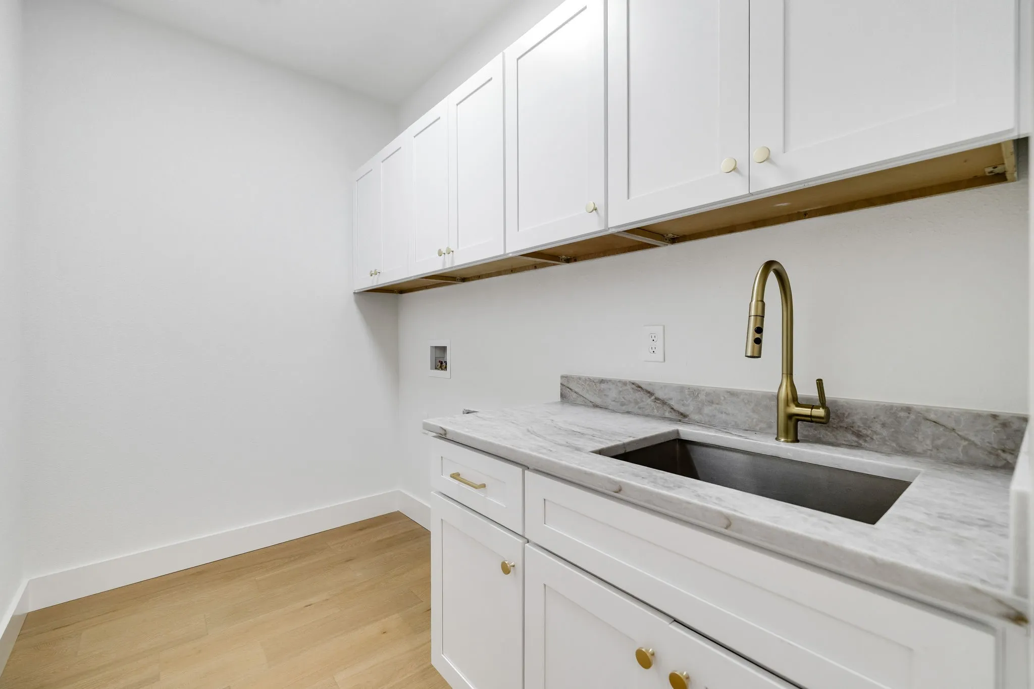 4402 Briargrove-White shaker cabinetry paired with wide-plank white oak flooring, an undermount sink, brass-tone fixtures, and Calacatta Taj quartz countertops.