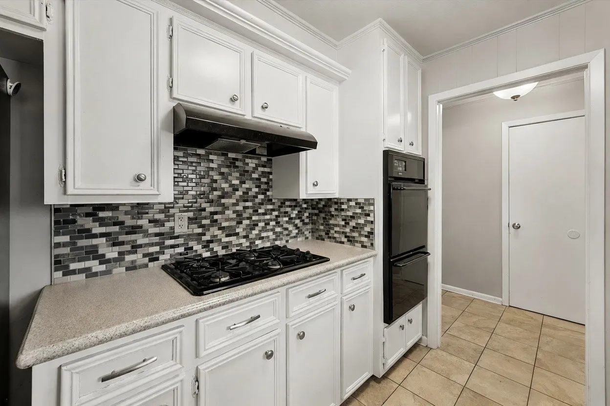 Clean galley kitchen features white cabinetry, neutral countertops, mosaic tile backsplash, gas cooking, and built-in storage in this Corsicana TX rental home.
