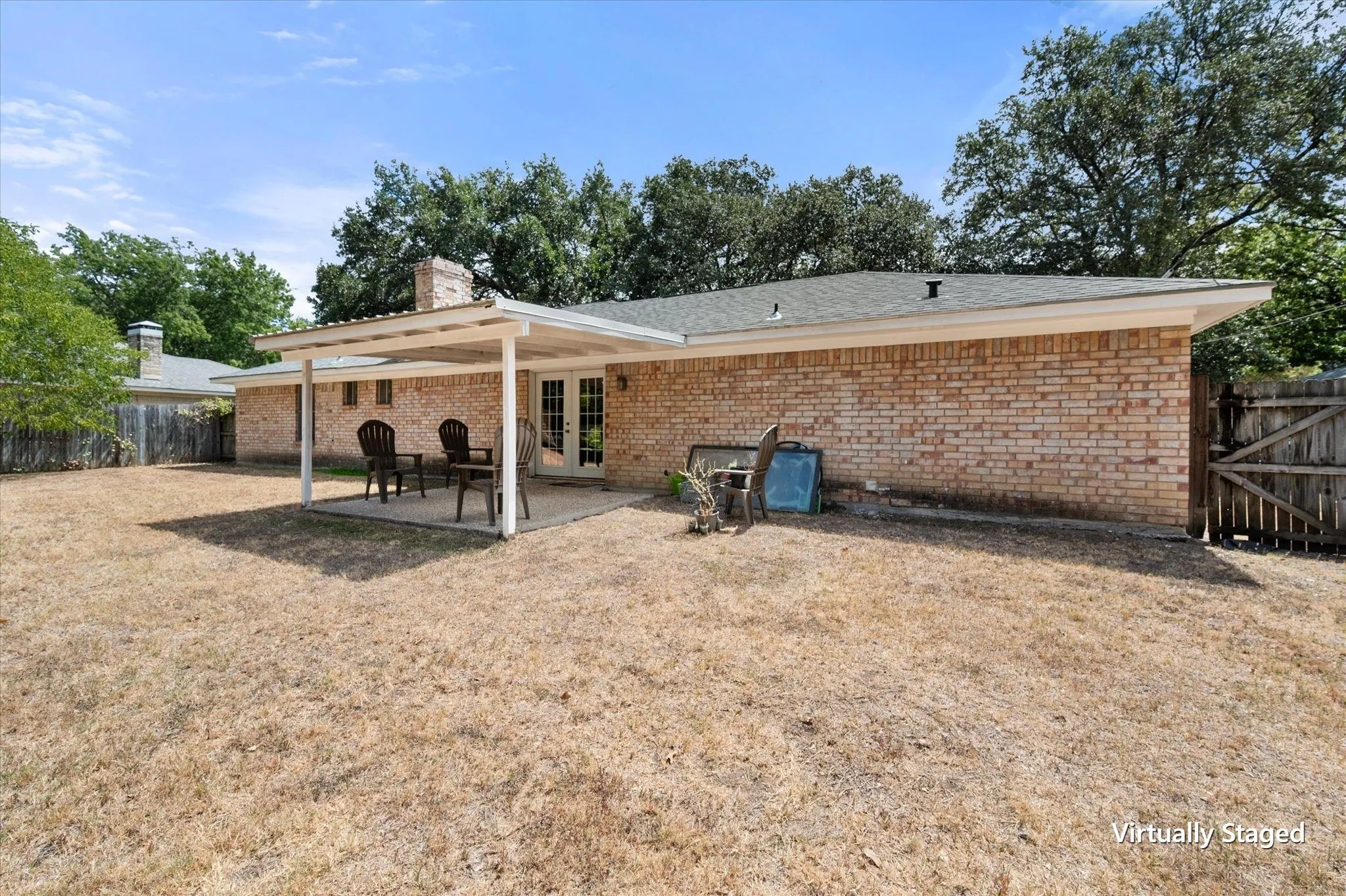 Rear exterior view showcases the home's brick construction, covered outdoor area, fenced yard, and generous backyard space.