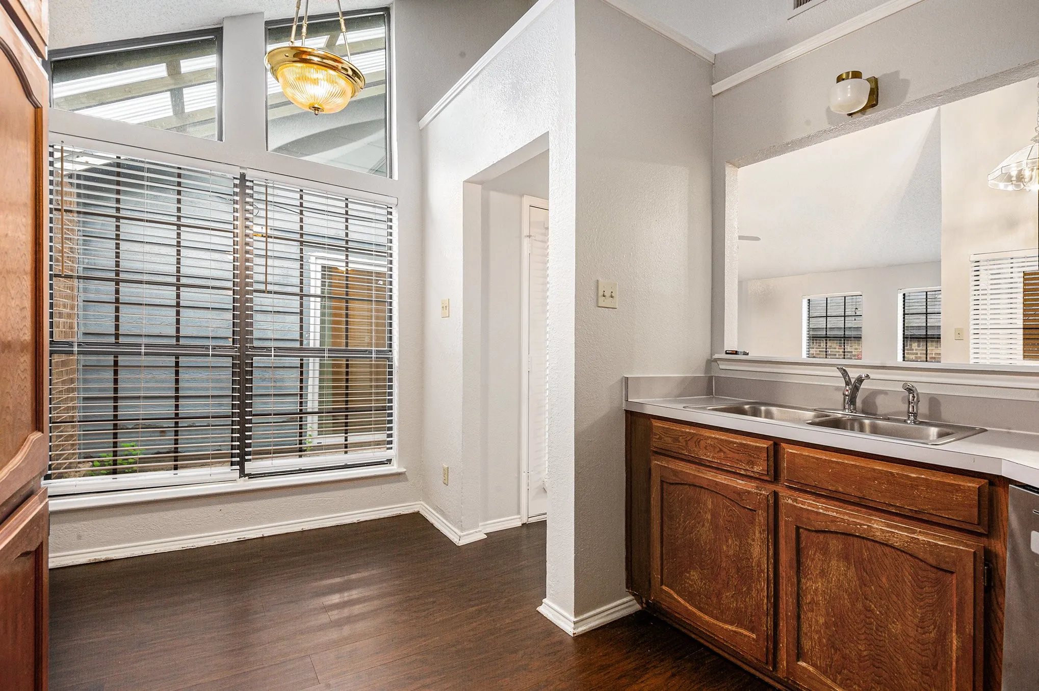 Kitchenette featuring rich wood cabinetry, a double basin sink with a chrome faucet, light-toned countertops, and wood-finish flooring